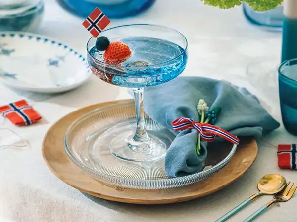 Kuvert med tretallerken, glasstallerken og coctailglass. Blått vannglass og flaggpynt.
