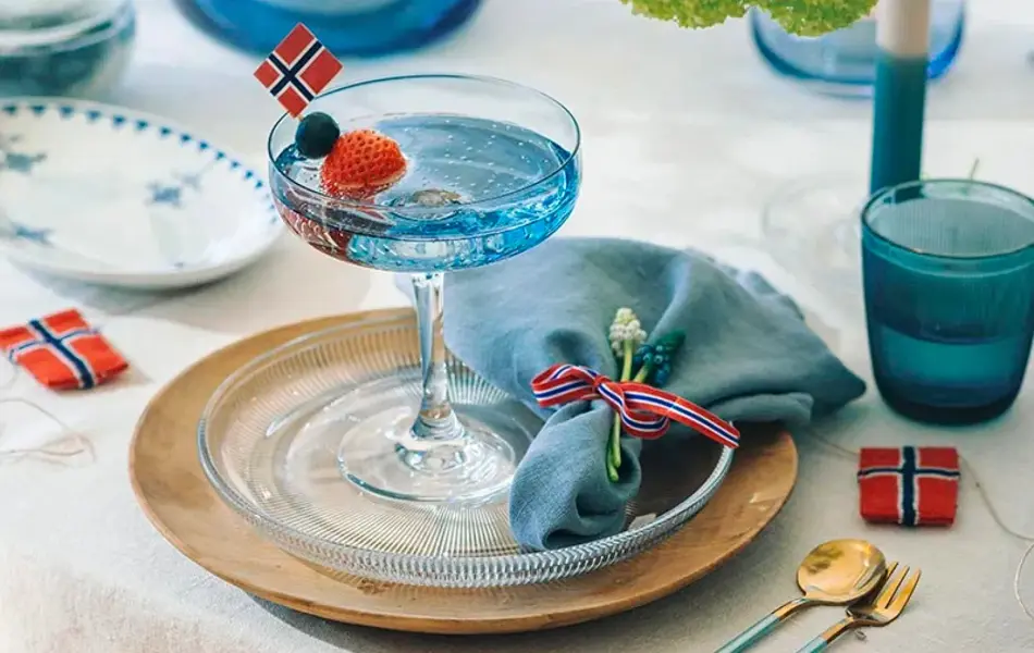 Kuvert med tretallerken, glasstallerken og coctailglass. Blått vannglass og flaggpynt.