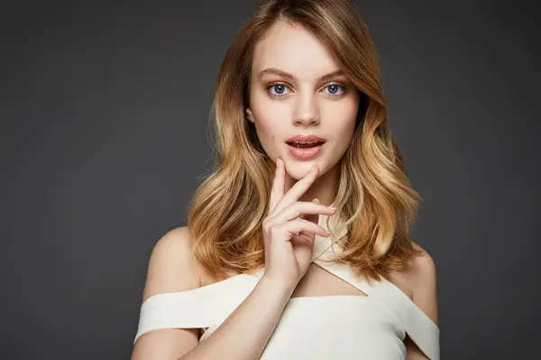 Kvinne med midtskill ser mot kamera, grå bakgrunn. Foto til artikkel om frisyrer til nyttårsaften.