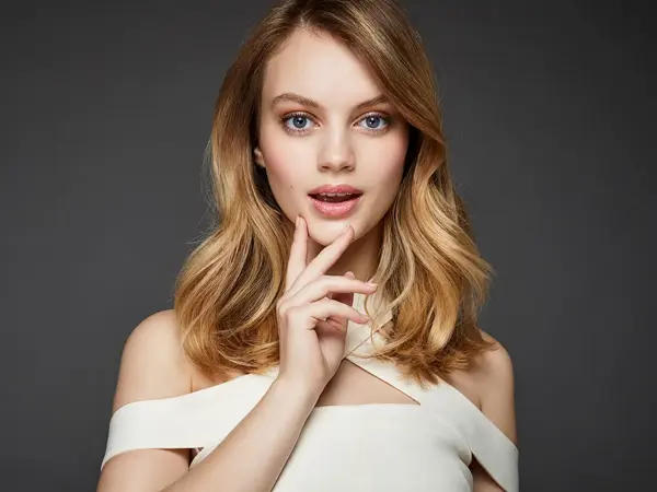 Kvinne med midtskill ser mot kamera, grå bakgrunn. Foto til artikkel om frisyrer til nyttårsaften.