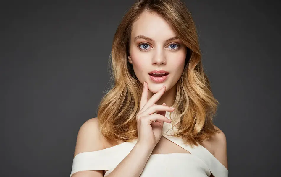 Kvinne med midtskill ser mot kamera, grå bakgrunn. Foto til artikkel om frisyrer til nyttårsaften.