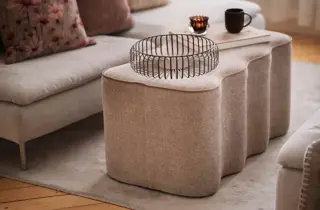 En beige puff brukt som bord med en kurv og noen pyntesaker på.