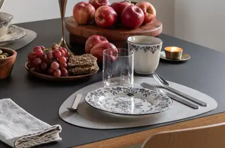 Dekketøy med tallerken, kopp og glass på et bord med frukt og snacks.