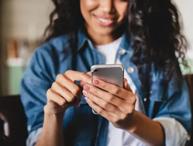 Cropped shot of an african-american young woman using smart phone at home.Smiling african american woman using smartphone at home, messaging or browsing social networks while relaxing on couch