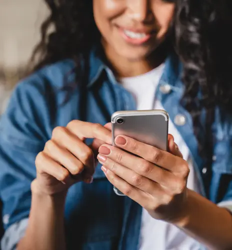 Cropped shot of an african-american young woman using smart phone at home.Smiling african american woman using smartphone at home, messaging or browsing social networks while relaxing on couch