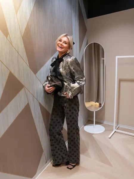 Dame med sølvbluse, sort sløyfe i halsen, sort bukse, sorte sko og liten paljettveske.