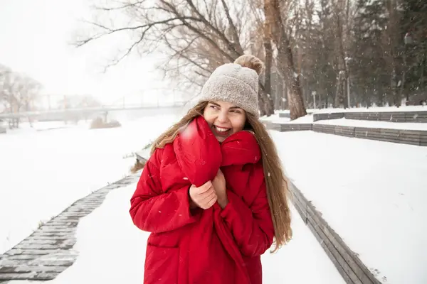 Jente med rød jakke og beige lue står ute i snøvær
