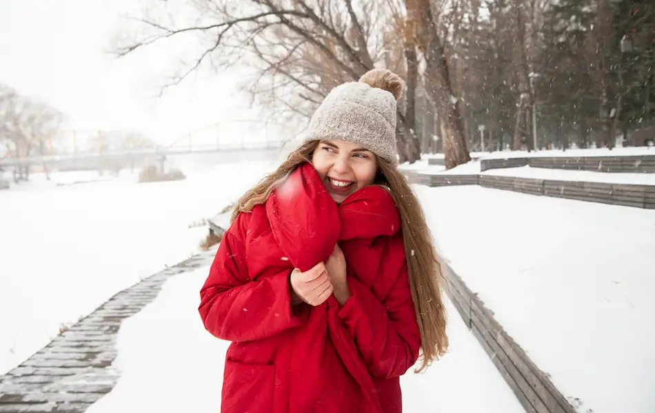 Jente med rød jakke og beige lue står ute i snøvær