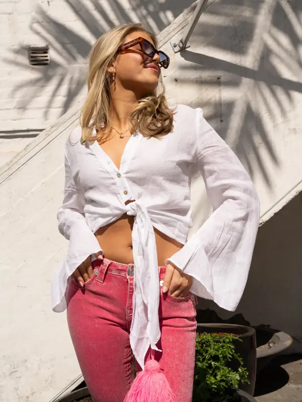 Jente står ute med solbriller, hvit kort skjorte-topp og rosa jeans.