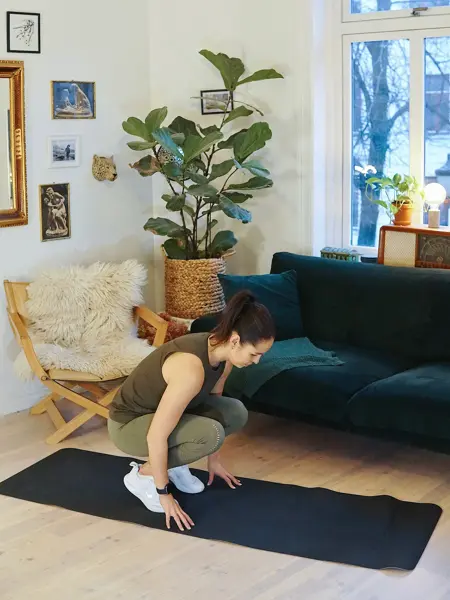 treningsekspert Anna Johansen trener på matte på gulvet, mørkegrønn sofa i bakgrunnen, lys stol med pels oppi, str grønn plante, bilder på veggen