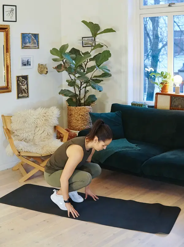 treningsekspert Anna Johansen trener på matte på gulvet, mørkegrønn sofa i bakgrunnen, lys stol med pels oppi, str grønn plante, bilder på veggen