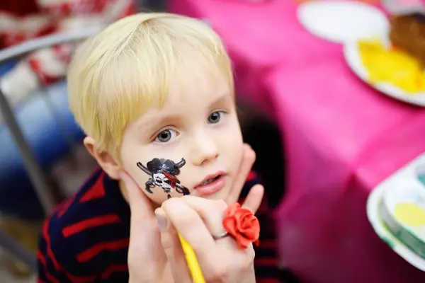 Face painting for cute little boy during kids merriment. Face paint for "Pirates" theme on birthday party. Preschooler kids celebrating party in entertainment center