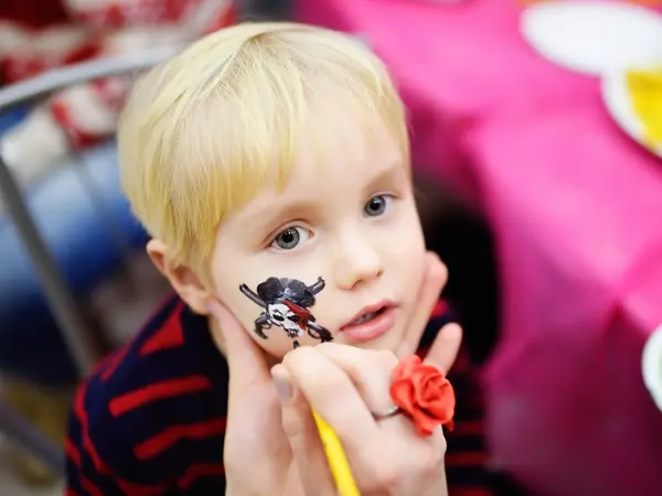 Face painting for cute little boy during kids merriment. Face paint for "Pirates" theme on birthday party. Preschooler kids celebrating party in entertainment center
