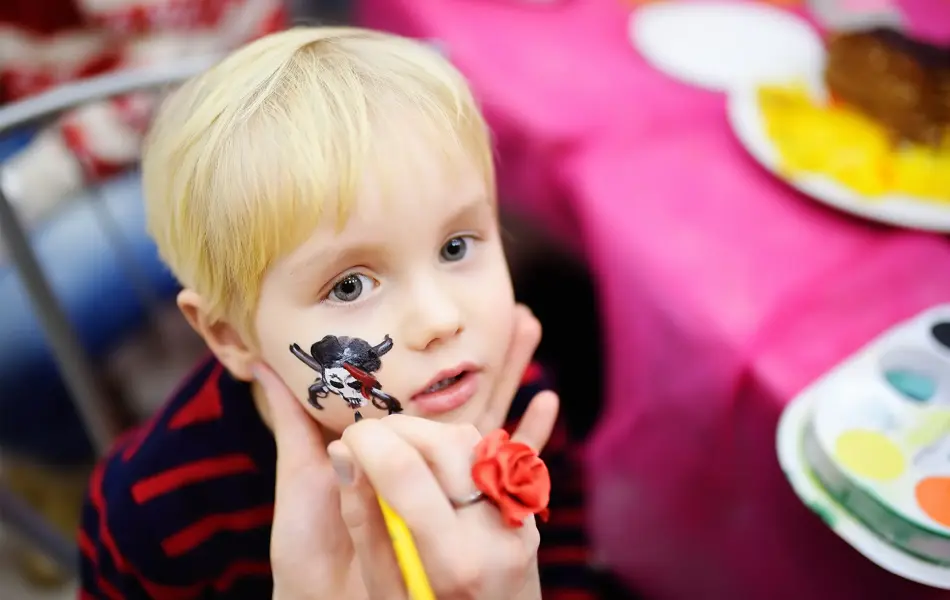Face painting for cute little boy during kids merriment. Face paint for "Pirates" theme on birthday party. Preschooler kids celebrating party in entertainment center