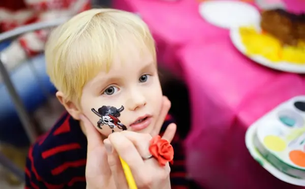 Face painting for cute little boy during kids merriment. Face paint for "Pirates" theme on birthday party. Preschooler kids celebrating party in entertainment center