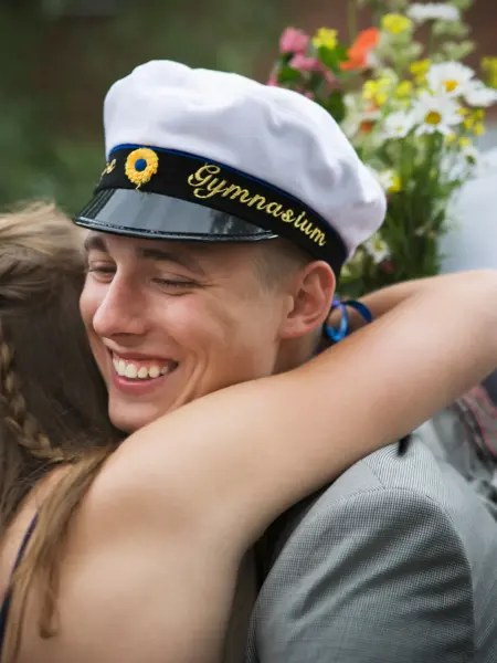 Videregående elev i studentlue klemmer kvinne