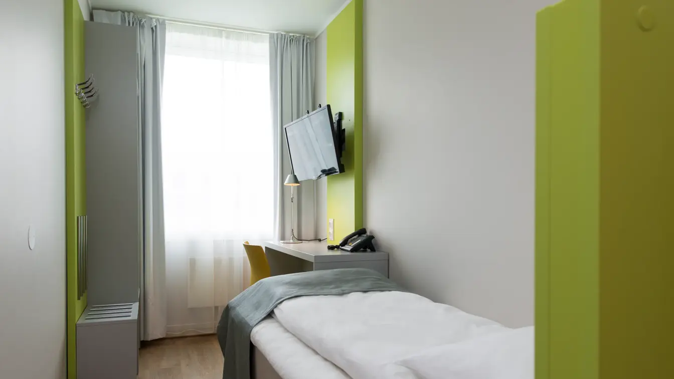 Small Single Room på Thon Hotel Trondheim. Hvite vegger med innslag av grønne flater. Oppredd seng, TV og lite skrivebord.