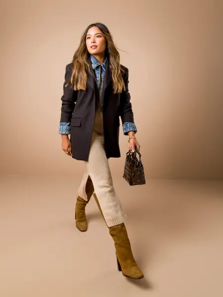 Tsustumi Hoang i mørk blå dressjakke, olaskjorte, beige skjørt, sort liten veske og brune semskede høye støvletter