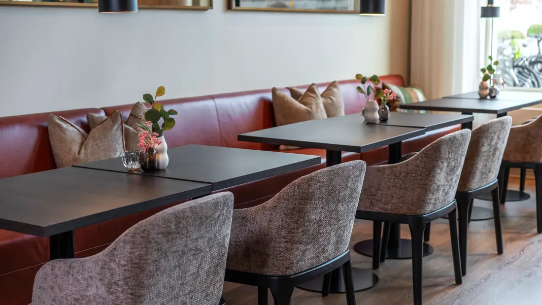 Sitteplasser i lobbyområde, med sittebenk langs veggen, sorte bord og tilhørende stoler