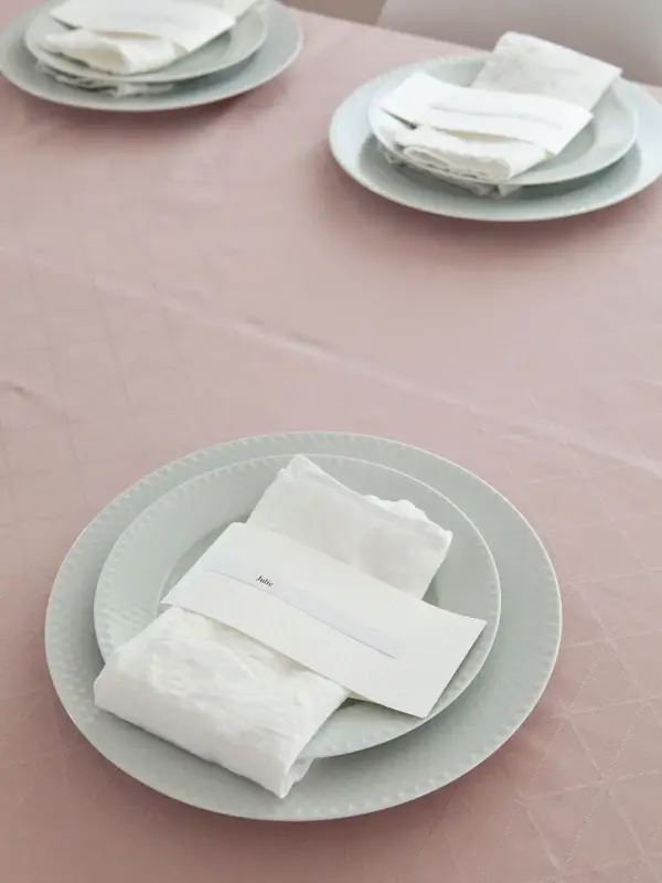 Steg 3 - Bord dekket med tallerkener og hvit linservietter og navnelapp på en rosa duk 