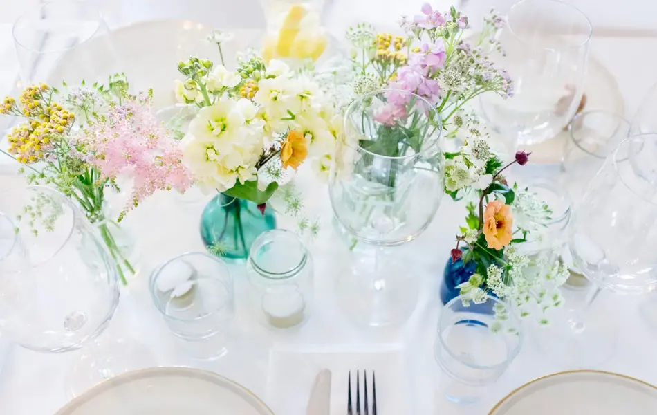 Hvitdekket bord dekorert med markblomster i små vaser