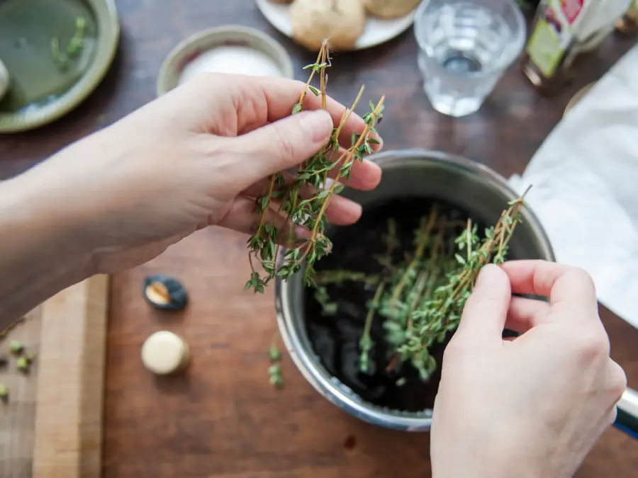 Woman adding fresh thyme leaves to a cooking pot filled with balsamic vinegar, to make a dressing. First person perspective.
