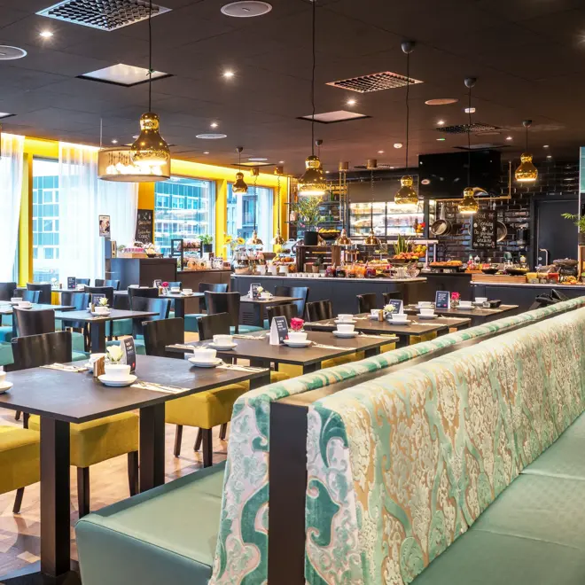 Restaurant med svarte spisebord, blå og gule stoler. vinduer fra gult til tak og store gule taklamper