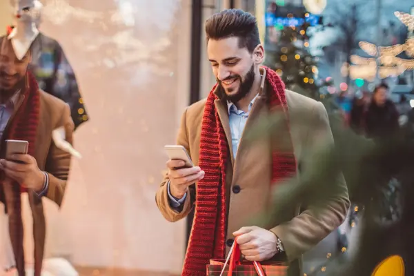 Young man holding  Christmas bags and checking his smart phone. Wearing warm clothing. Vienna, Austria.