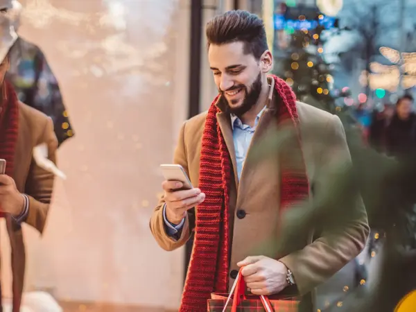 Young man holding  Christmas bags and checking his smart phone. Wearing warm clothing. Vienna, Austria.
