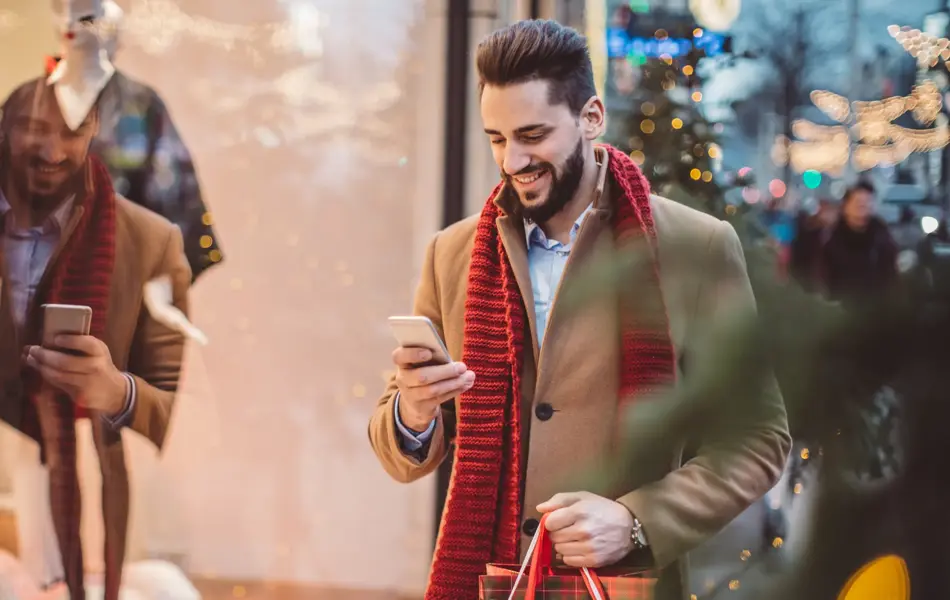 Young man holding  Christmas bags and checking his smart phone. Wearing warm clothing. Vienna, Austria.