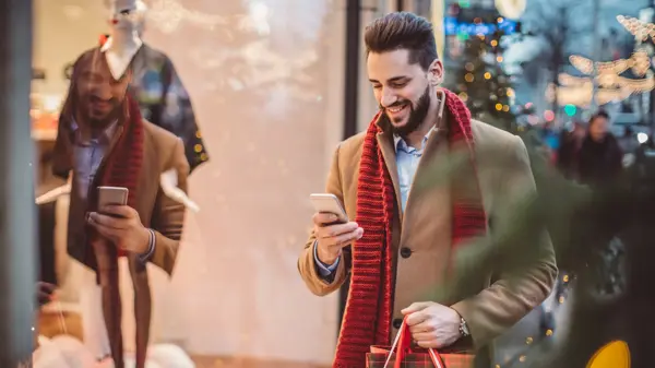 Young man holding  Christmas bags and checking his smart phone. Wearing warm clothing. Vienna, Austria.
