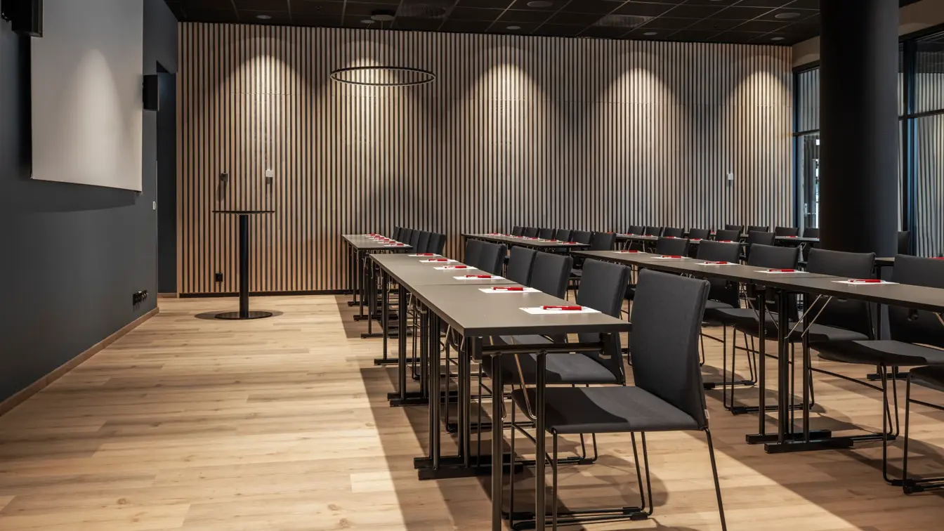 Konferanserom med klasserom oppsett, parkett, mørke farger på interiør, stort lerret på fremste vegg