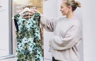 Dame holder opp en kjole med grønt blomstermønster utenfor en bruktbutikk