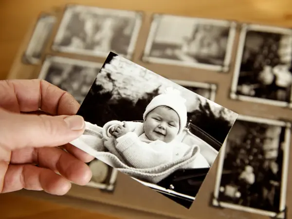 Mature person's hand holding sepia toned 1950s style photograph of young baby in pram