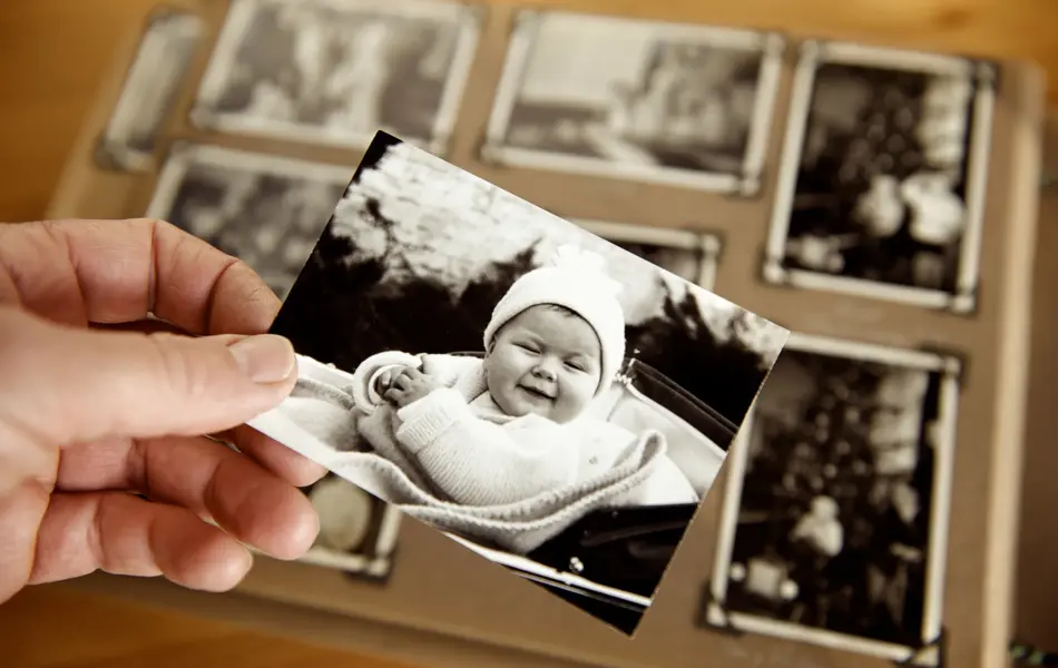 Mature person's hand holding sepia toned 1950s style photograph of young baby in pram