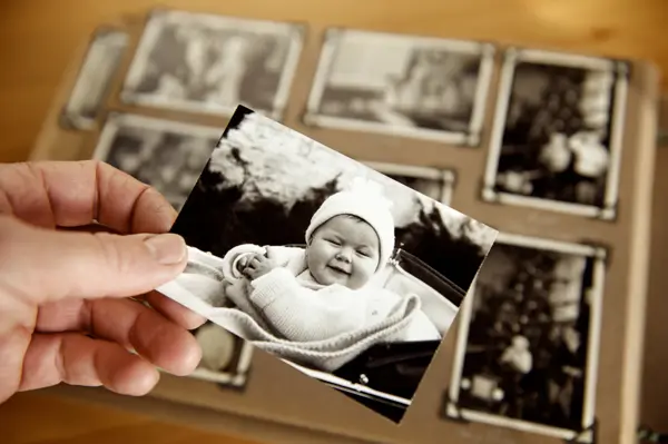 Mature person's hand holding sepia toned 1950s style photograph of young baby in pram