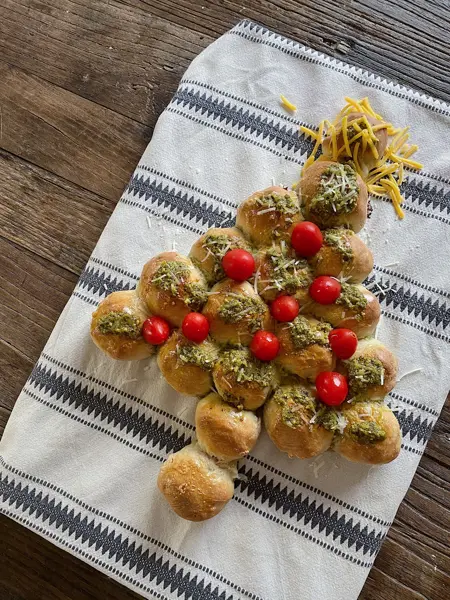 Et brett med et spiselig juletre laget av boller, pyntet med tomater, pesto og ost