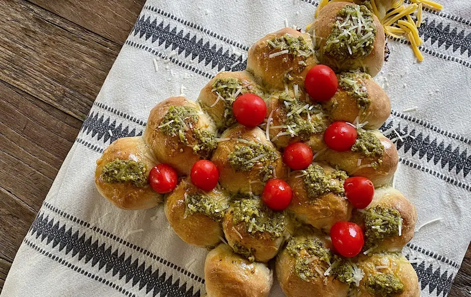 Et brett med et spiselig juletre laget av boller, pyntet med tomater, pesto og ost