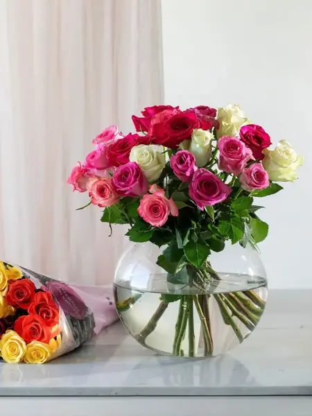 Rosebukett i en vase på et bord med bukett roser liggende ved siden av