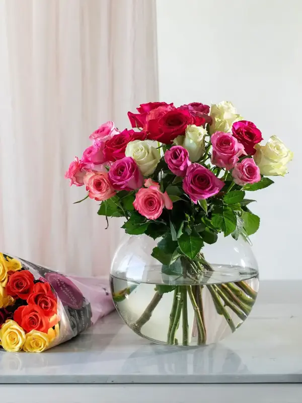 Rosebukett i en vase på et bord med bukett roser liggende ved siden av