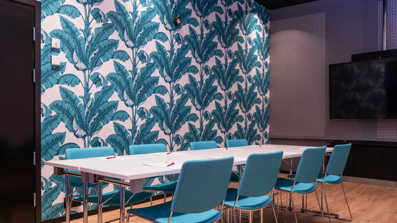 Fargerik tapet med turkise blad, turkise stoler og hvitt bord i møterom på Thon Hotel Storo i Oslo.