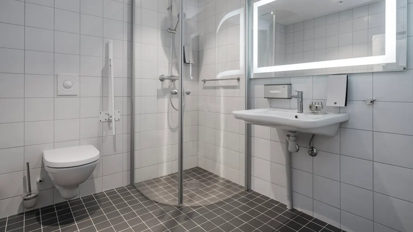 Dusj, toalett og vask med god gulvplass og støttearmer rundt toalett på  handikaprom på Thon Hotel Lofoten
