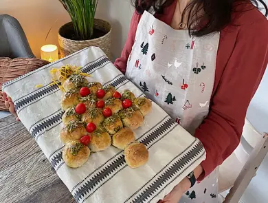 Utsnitt av en kvinne som holder opp et bakebrett med et spiselig juletre laget av boller