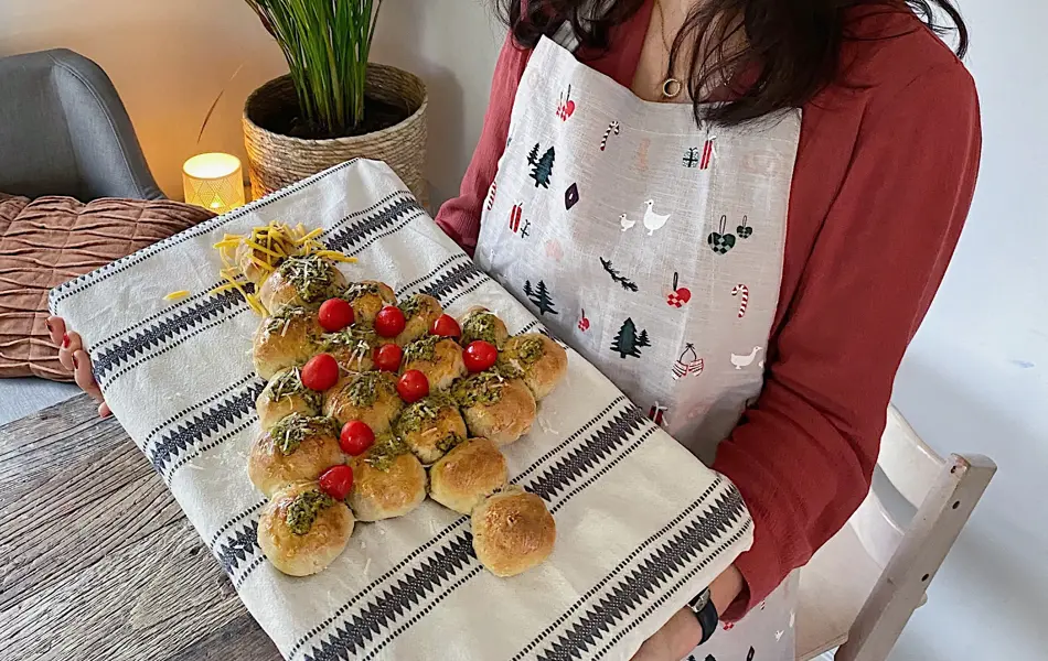 Utsnitt av en kvinne som holder opp et bakebrett med et spiselig juletre laget av boller