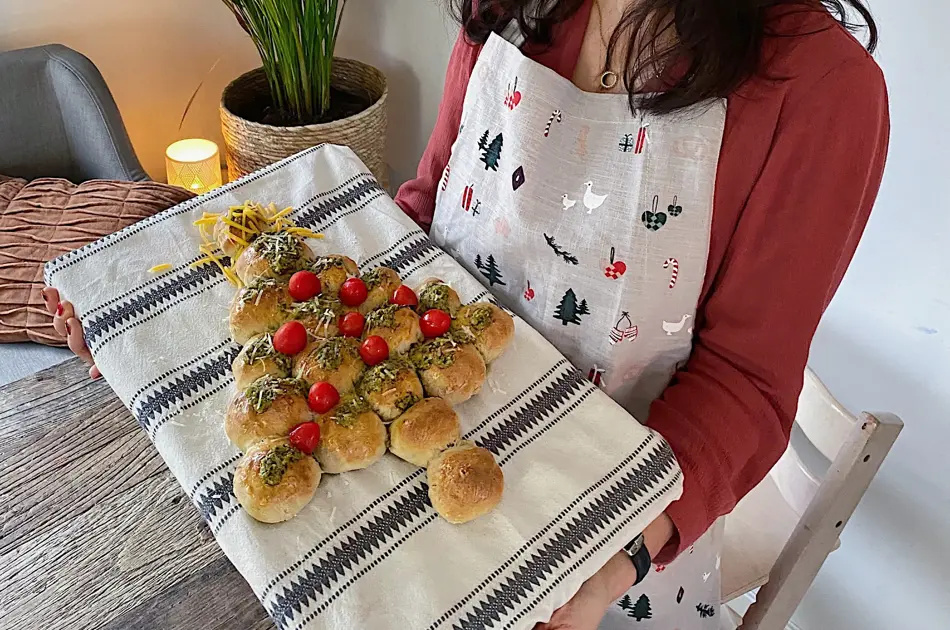 Utsnitt av en kvinne som holder opp et bakebrett med et spiselig juletre laget av boller