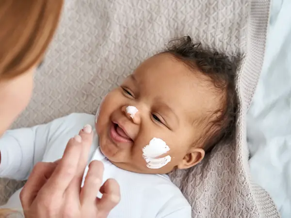 Caucasian mother applying healthy skin care moisturizing cream on cute adorable funny african american baby girl daughter face. Skincare lotion for infant pediatric diathesis treatment concept.