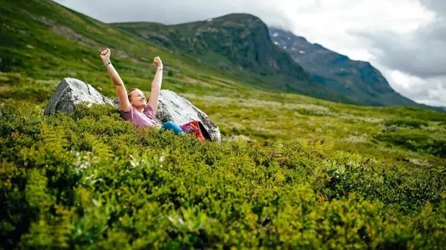 Dam som strekker armene i været i en grønn eng på fjellet 