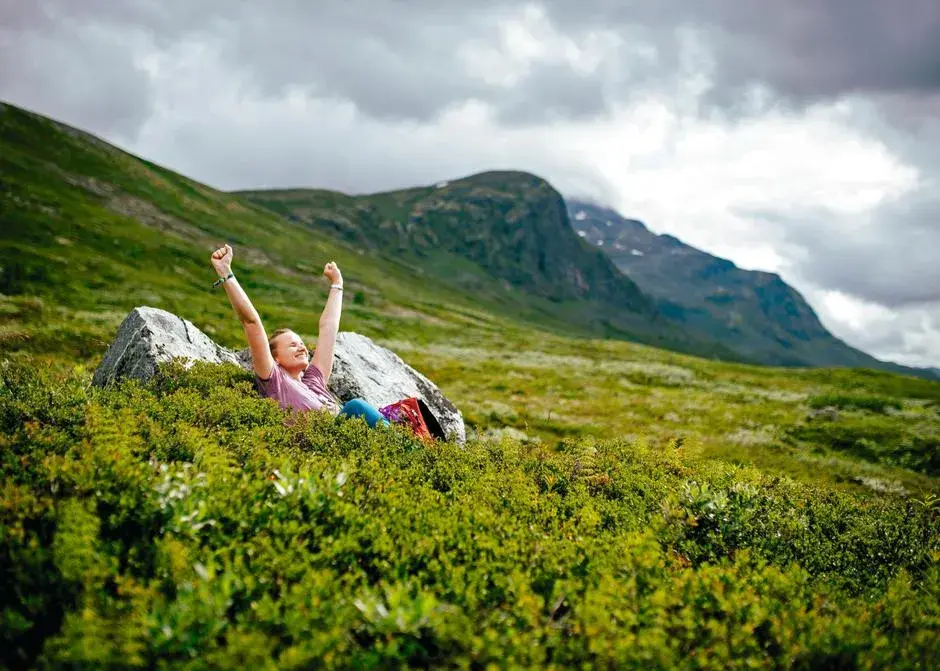 Dam som strekker armene i været i en grønn eng på fjellet 