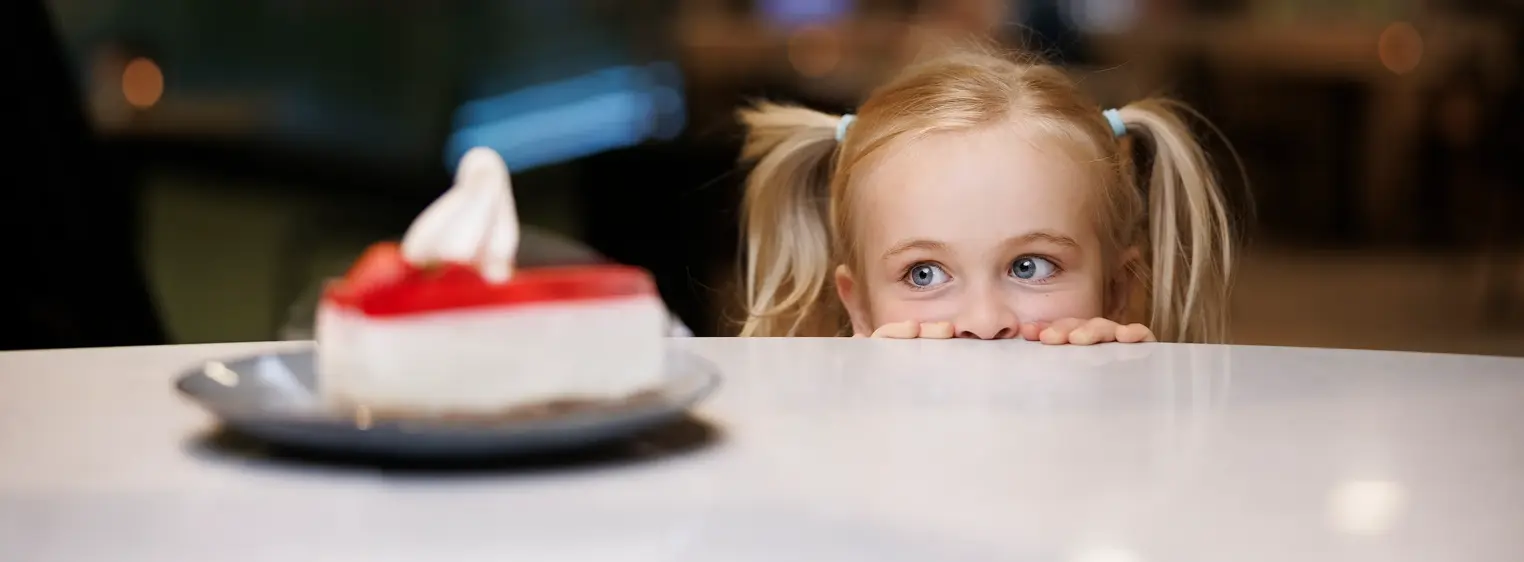 En liten jente som titter over et bord på en kakebit som står på bordet