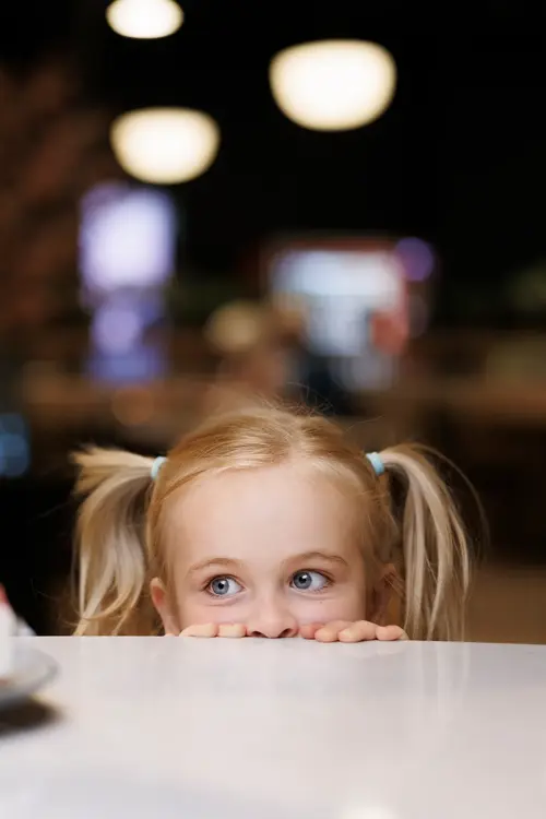 En liten jente som titter over et bord på en kakebit som står på bordet